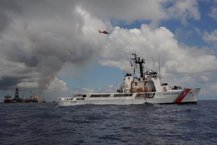 A USCG HH-65 Dolphin helicopter flies overhead as the Coast Guard Cutter Resolute steams near Deepwa